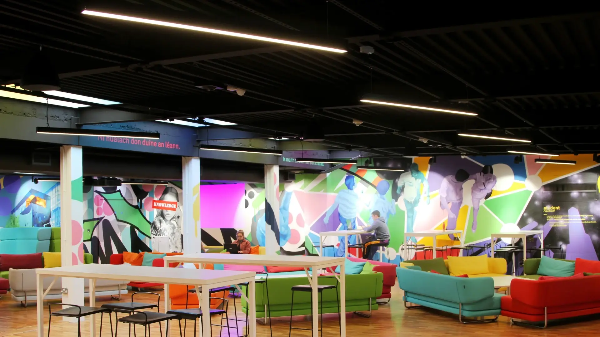 LED lighting system shines over a university lounge with tables and bright coloured walls