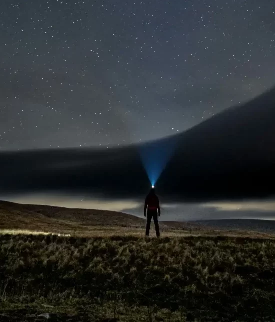 A man wearing a head torch in a field under a starry sky as part of astrotourism.