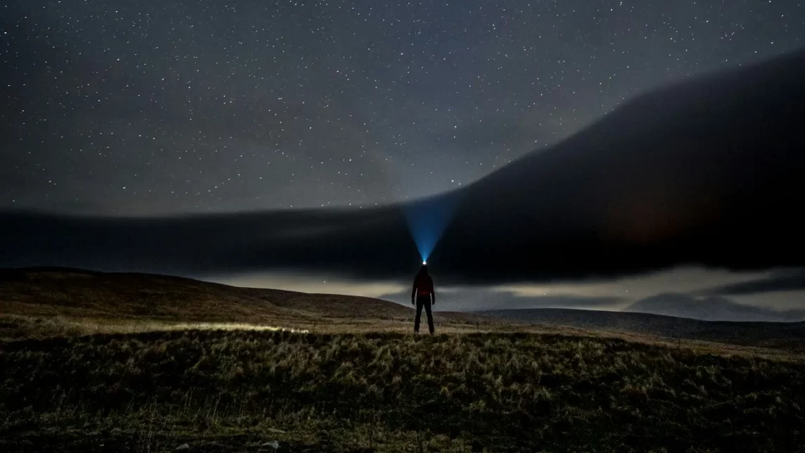 A man wearing a head torch in a field under a starry sky as part of astrotourism.