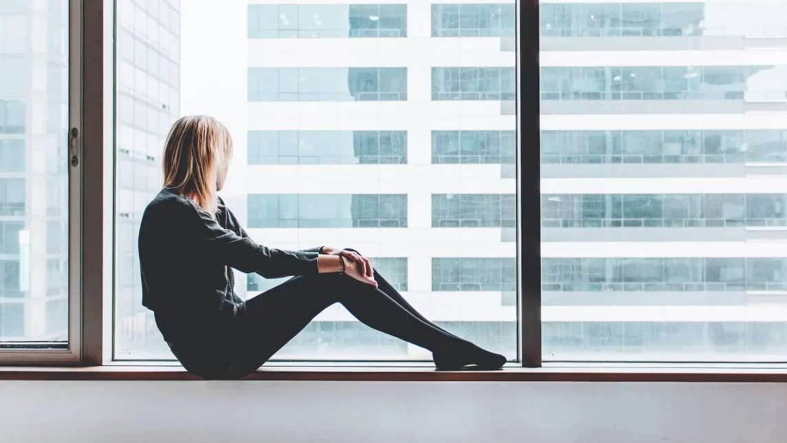 Woman sat on a window ledge looking out